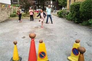 A girl throws a ball at a coconut shy as her family look on