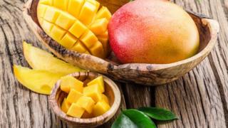Wooden bowl with half a chopped mango and one whole mango