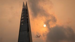 Самолет пролетает мимо Осколка в центре Лондона, когда небо приобретает необычный оранжевый цвет