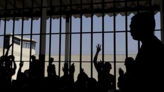 Pessoas contra as grades de presídio