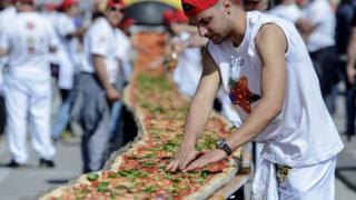 A man adds topping to the giant pizza in Naples.