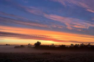 View of sunrise over fields with morning mist