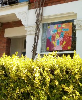A colour picture in a window behind a hedge