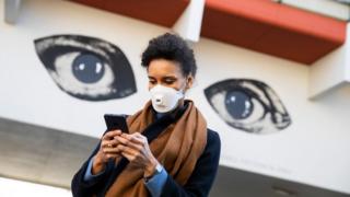 Woman using smartphone by graffiti of two eyes