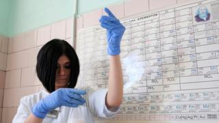 Mujer en un laboratorio con la tabla periódica colgada en la pared