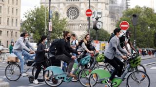 Bikers wearing protective masks ride past Notre Dame Cathedral