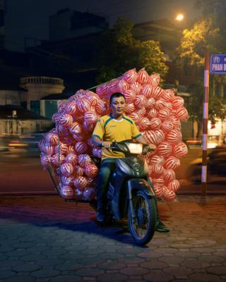 A man posed on a motorcycle with hundreds of red and white coloured bouncy attached to the back