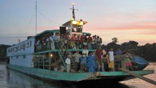A ferry full of people travels along a river in Amazonian Peru