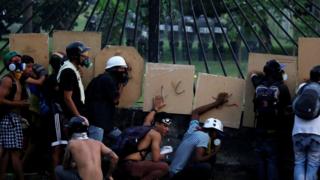 Военные (на заднем плане) занимают позиции на авиабазе в Каракасе, когда митингуют сторонники оппозиции