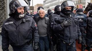 officers in riot gear flanking an elderly man