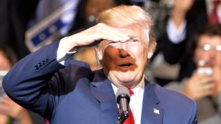 Дональд Трамп поднимает руку, чтобы защитить глаза от яркого луча света