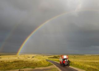 A rainbow is seen in the countryside as an old-fashioned bus drives by