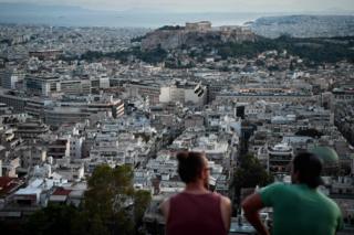 Young men sit on a hill overlooking the city of Athens, 8 August 2018