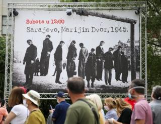 Menschen marschieren an einem Plakat vorbei, das Nazi-Opfer während des Zweiten Weltkriegs zeigt