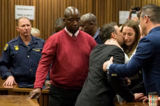 South African Paralympian athlete Oscar Pistorius (centre) holds his sister Aimee Pistorius as he leaves the High Court in Pretoria