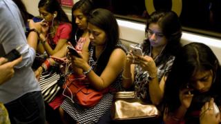 Women listen to smartphones on the metro in Delhi