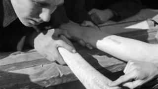 Un niño observa los números tatuados en los brazos de otro prisionero en el campo de concentración de Dachau.