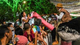 An artist poses for a child taking photos of the "ostrich" she sits astride of