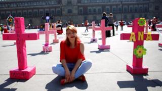 A woman sits among pink crosses during the 