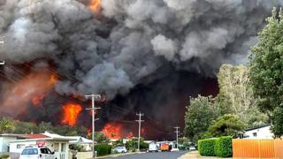 science Massive flames and smoke clouds from a major bushfire hang over a suburban street in Harrington, New South Wales