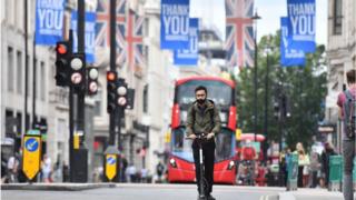 Man in mask on a scooter riding down Oxford Street with Thank you banners hanging from lampposts
