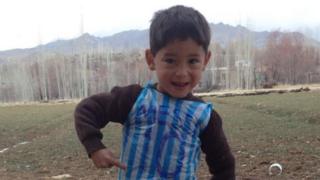 Photo of Murtaza Ahmadi wearing a plastic carrier bag with blue and white stripes. 'Messi' and the number '10' is written in marker