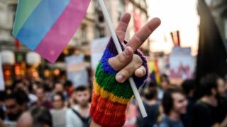 LGBT yürüyüşünde zafer işareti yapan bir el gökkuşağı renklerinden bir bayrak tutuyor.