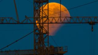 The moon standing in a partial lunar eclipse can be seen behind a constructin crane on August 7, 2017 in Gilching, southern Germany.