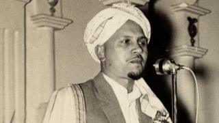 Portrait en noir et blanc de l'imam Haron s'adressant à un auditoire avec un microphon