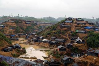 Vista de un campo de refugiados con muchas casas improvisadas de bambú y lonas. Está inundado por las lluvias.