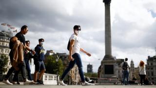 Des personnes portant des masques protecteurs traversent Trafalgar Square