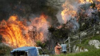 Two neighbours look at the flames as firefighters work to extinguish a forest fire at Ribera de Arriba in Asturias