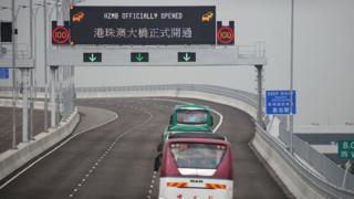 Buses pass a sign on the Hong Kong-Zhuhai-Macau Bridge off Hong Kong