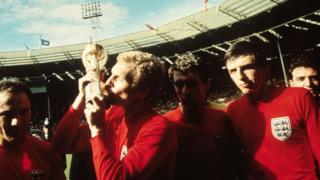 Bobby Moore, wearing red, holding the World Cup in 1966
