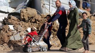 A family - including a child in a pushchair - walk past rubble