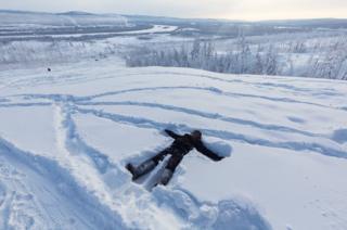 Аяль лежит в снегу на вершинах Верхоянска, ожидая, когда его мать и некоторые из ее друзей поднимутся на холм. На заднем плане виден дым, выходящий из угольных электростанций поселка.