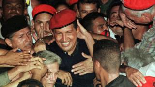   Chavez still young, red beret, smiling, kissed by apiadores 