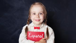 Niña sostiene un libro con la palabra español.