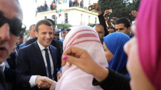 Президент Франции Эммануэль Макрон приветствует людей на улицах Алжира 6 декабря 2017 года. Макрон начал свою первую официальную поездку в Алжир, объявив, что он приезжает как «друг», несмотря на исторически колючие отношения Франции с ее бывшей колонией.
