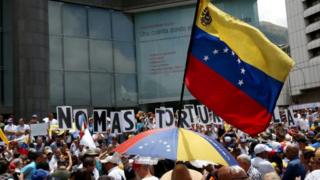 Bandera de Venezuela y detrás unos carteles que dicen "No más torturas".