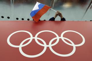 Torcedor com bandeira russa diante de logo olímpico