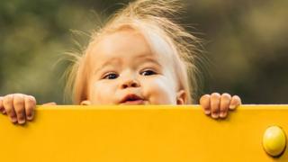 niña asomándose detrás de una tabla.