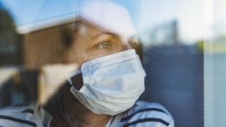 Woman looking out of window wearing a mask