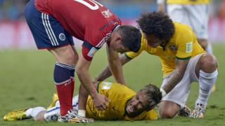 Neymar está en el suelo quejándose de dolor y sus compañeros intentan incorporarlo.