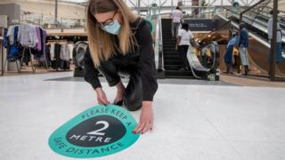 Woman wearing face mask sticks social distancing sticker to John Lewis floor