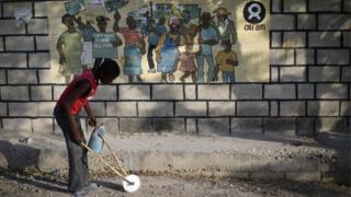 Мальчик, играющий с самодельной игрушкой, проходит мимо знака Oxfam в Порт-о-Пренсе, Гаити,