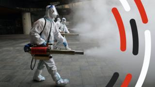 A person in a hazmat suit sprays disinfectant