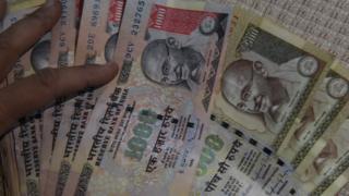Индийская жительница держит в своем доме в Нью-Дели банкноты 500 и 1000 индийских рупий 8 ноября 2016 года.