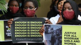 Protesters wearing face masks hold banners saying "enough is enough" and "justice in Nigeria for women and girls".