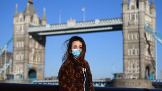 A member of the public poses for a photo in front of Tower Bridge whilst wearing a protective mask on March 22, 2020 in London.